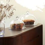 This Vienna Glass Dome and Plate 25 cm by LSA has a rounded dome shape with clear mouth-blown glass and a rounded handle.