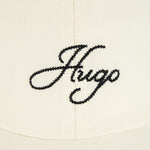 Close up of the Hugo logo on the front of the BOSS Ally Cream Cotton-Twill Cap with Embroidered Edges and Hugo Logo.